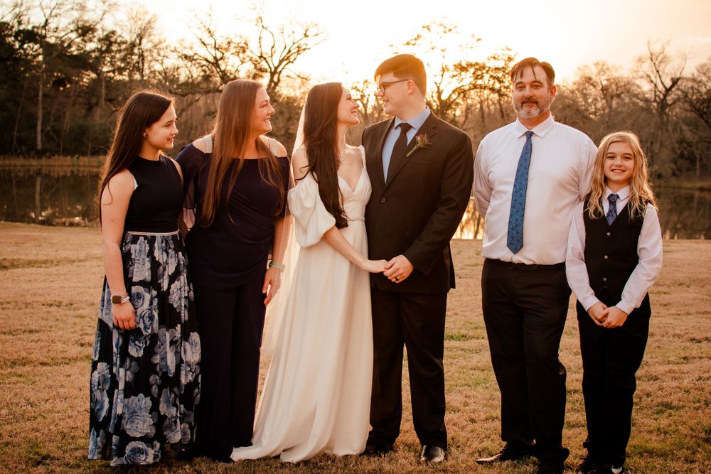 Wedding party gathered outdoors at sunset with formal attire.