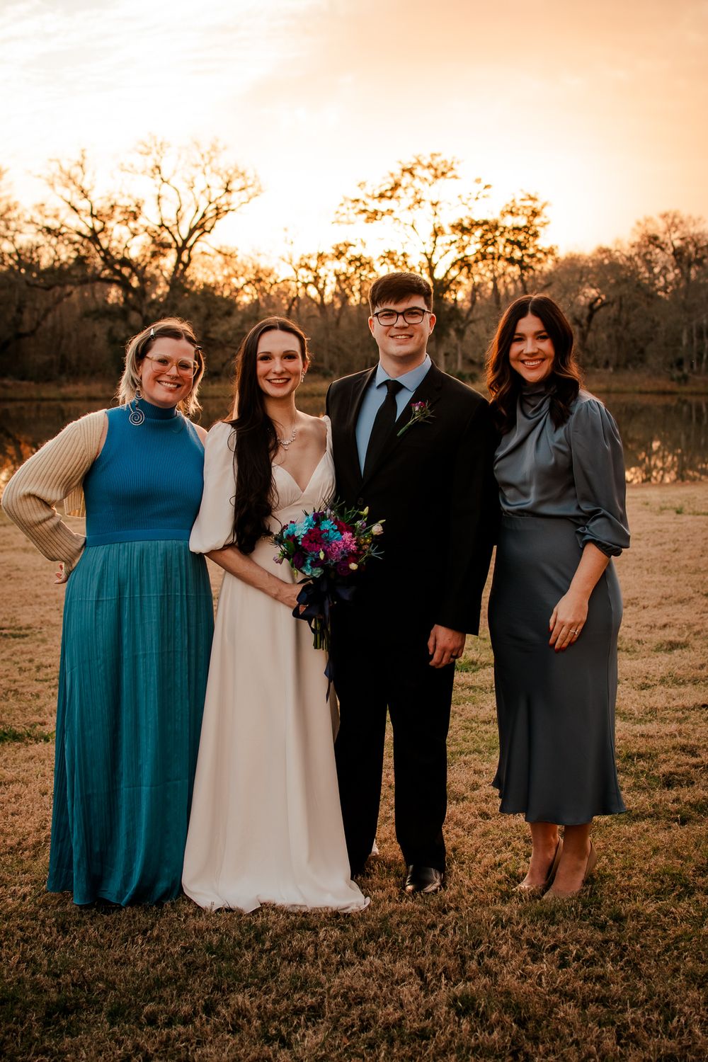 Wedding party poses at sunset near a lake with vibrant fall colors in the background.
