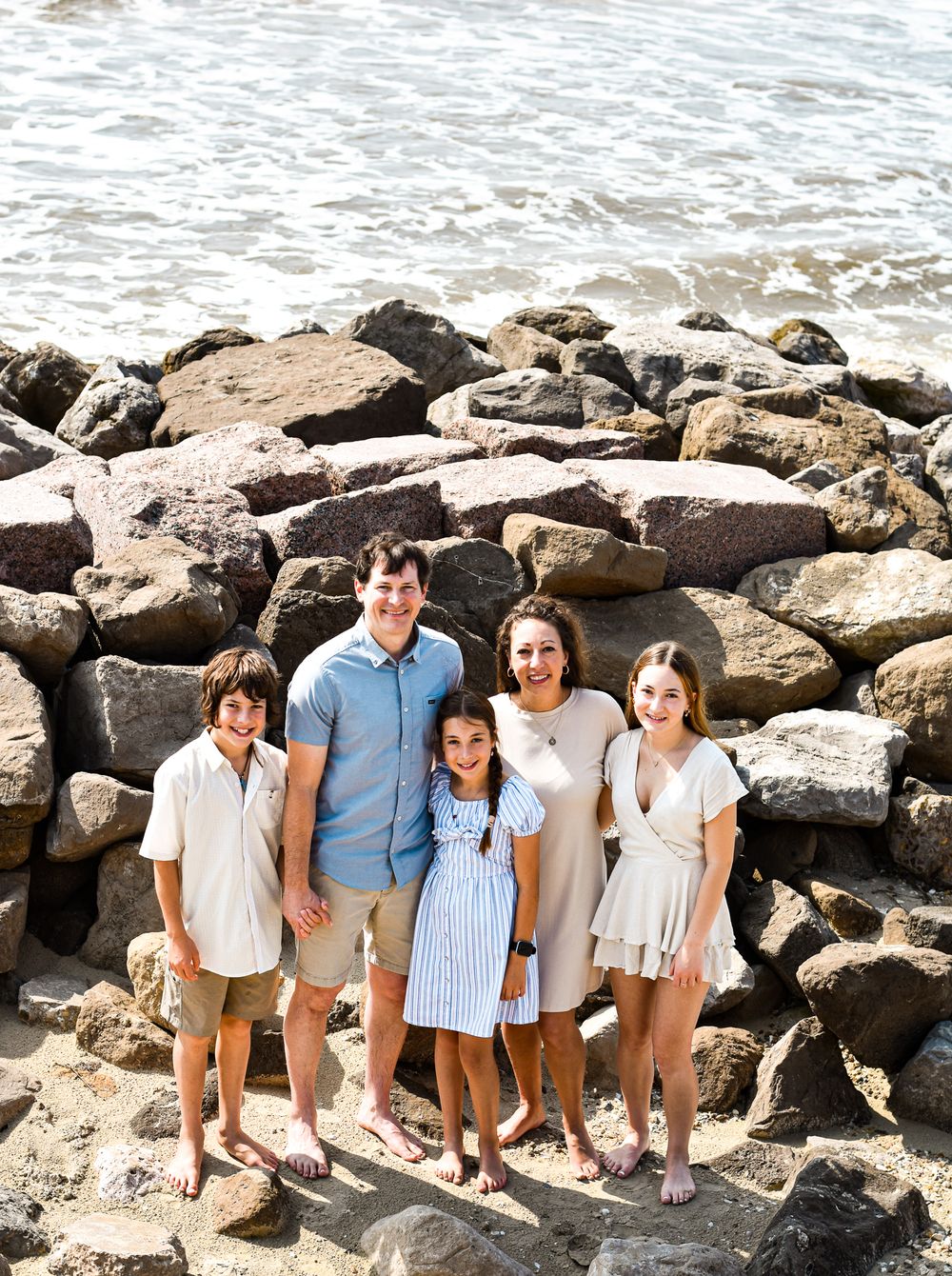 A family poses together on rocky beach terrain with ocean waves in the background.