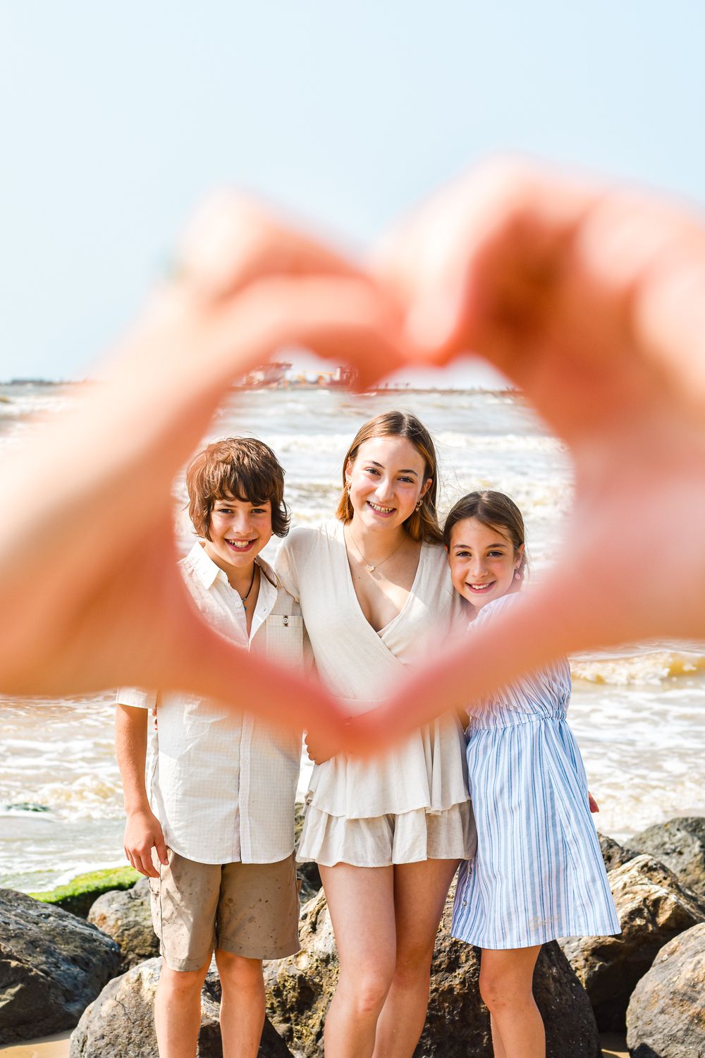 Hands forming heart shape frame around family posing on rocky beach.