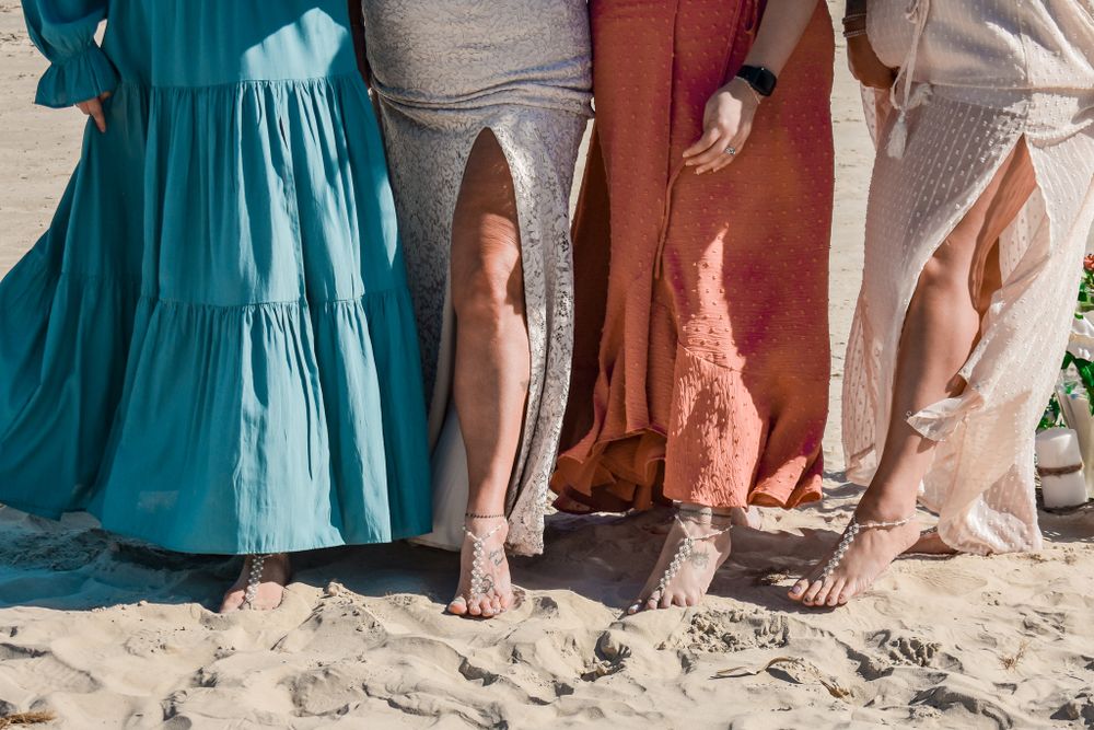 Row of flowy dresses and bare feet standing in beach sand.