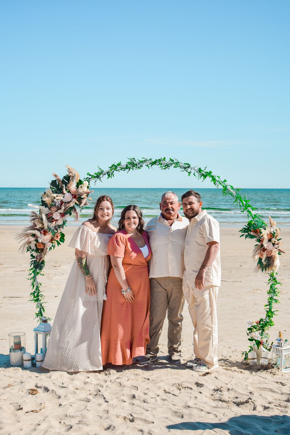 Beach wedding photo with floral arch decor and turquoise ocean backdrop.