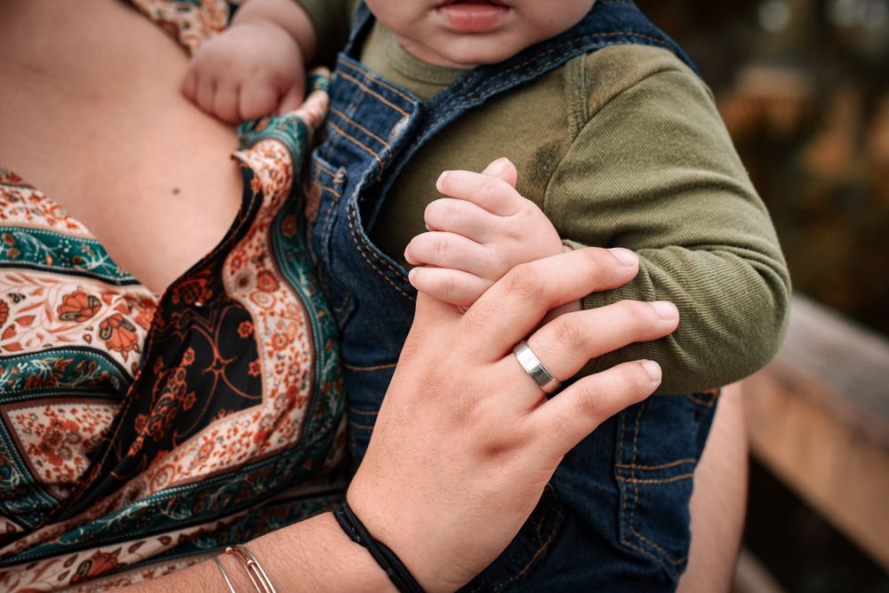 Close-up of hands holding toddler wearing blue overalls and green shirt.