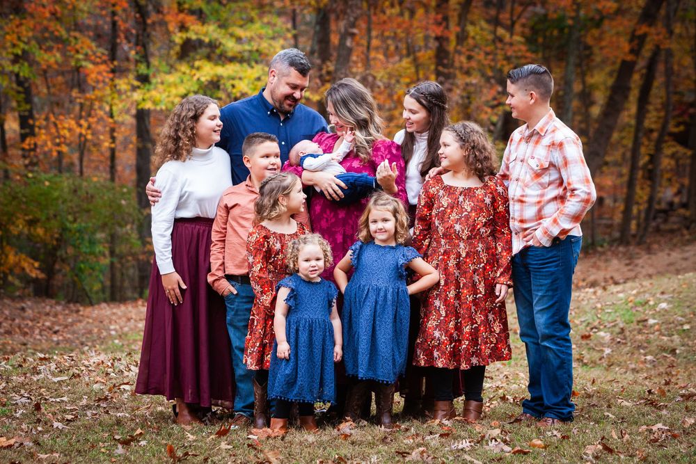 Large family with multiple children poses together outdoors among colorful autumn foliage.