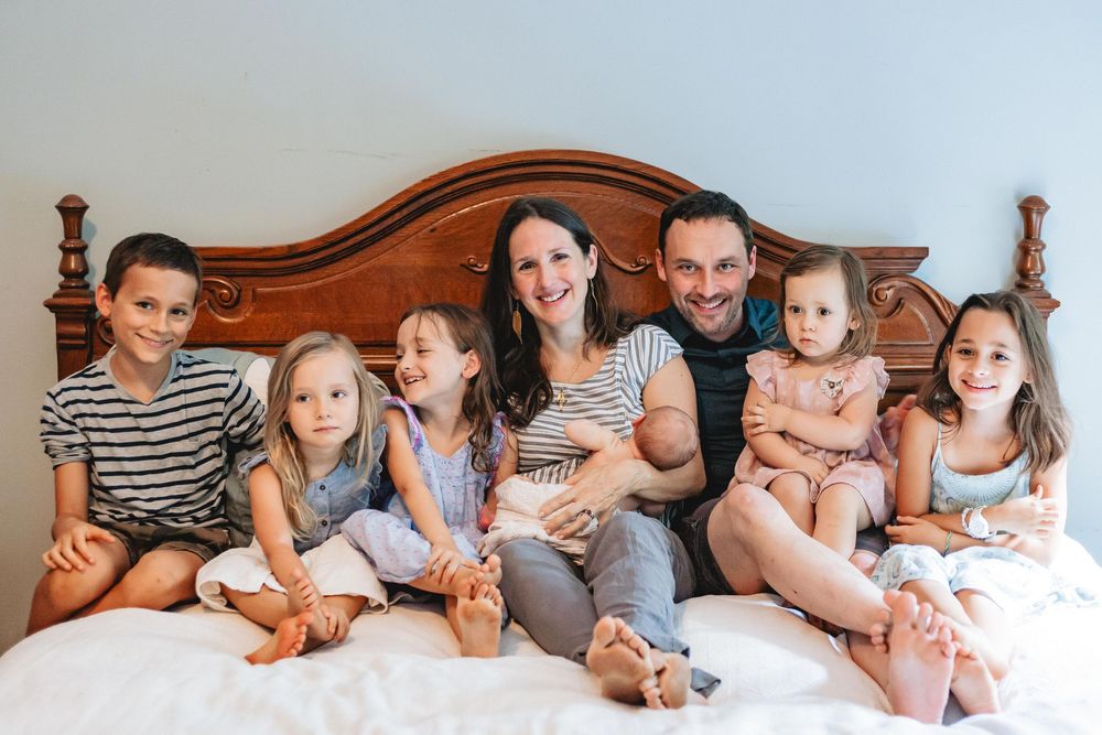 Happy family of seven with five children and parents posing together on a white bed.