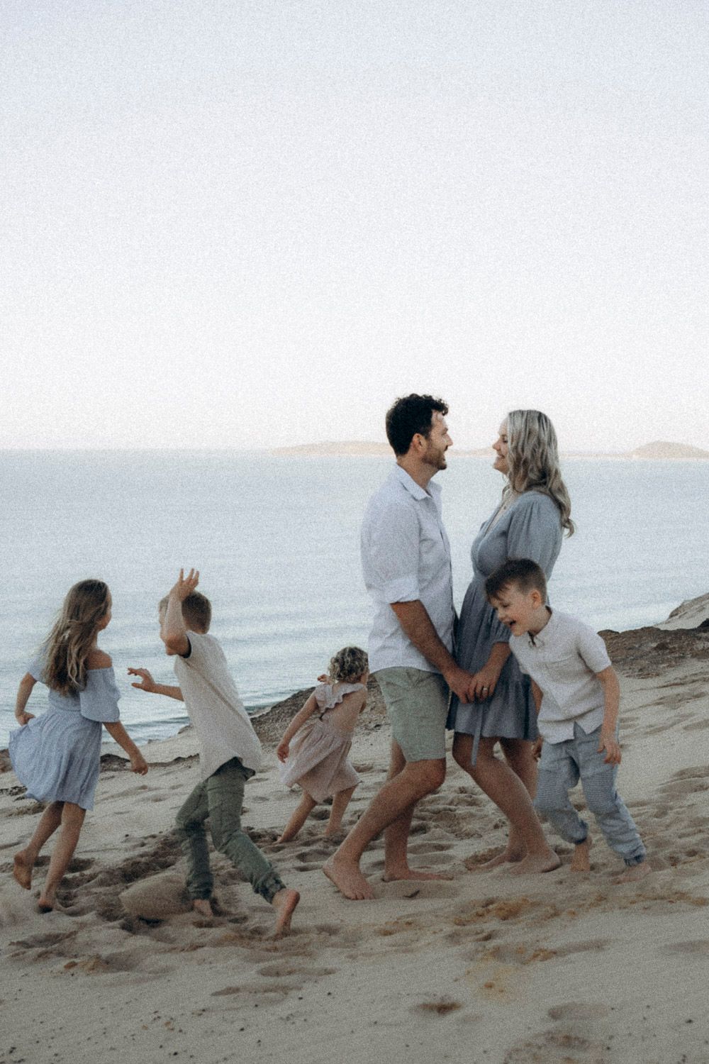 A family plays together in sequence photos on a sandy beach at sunset with mountains visible in the distance.