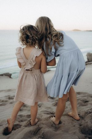 Children in light coloured dresses exploring and playing together on a sandy beach.