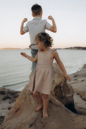 Children climbing and playing on sandy rock formations near the ocean.