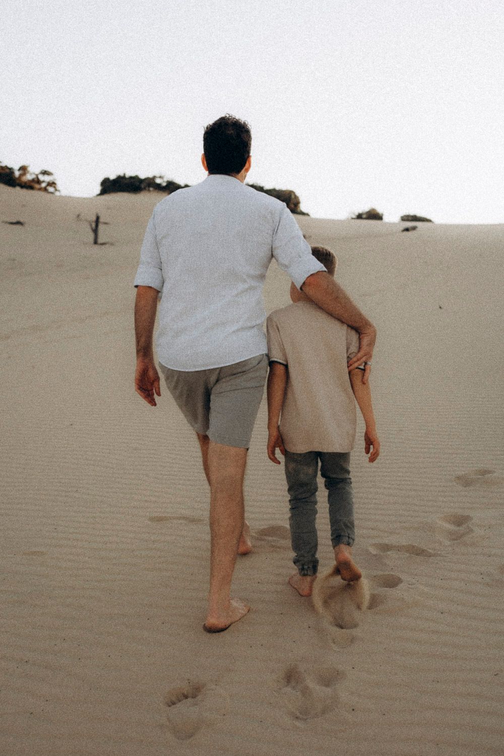 Two people walking up a sandy desert dune leaving footprints behind in a sequence of progressive movement shots.