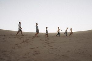 Silhouettes of people walking and playing on a sandy hill against the horizon.