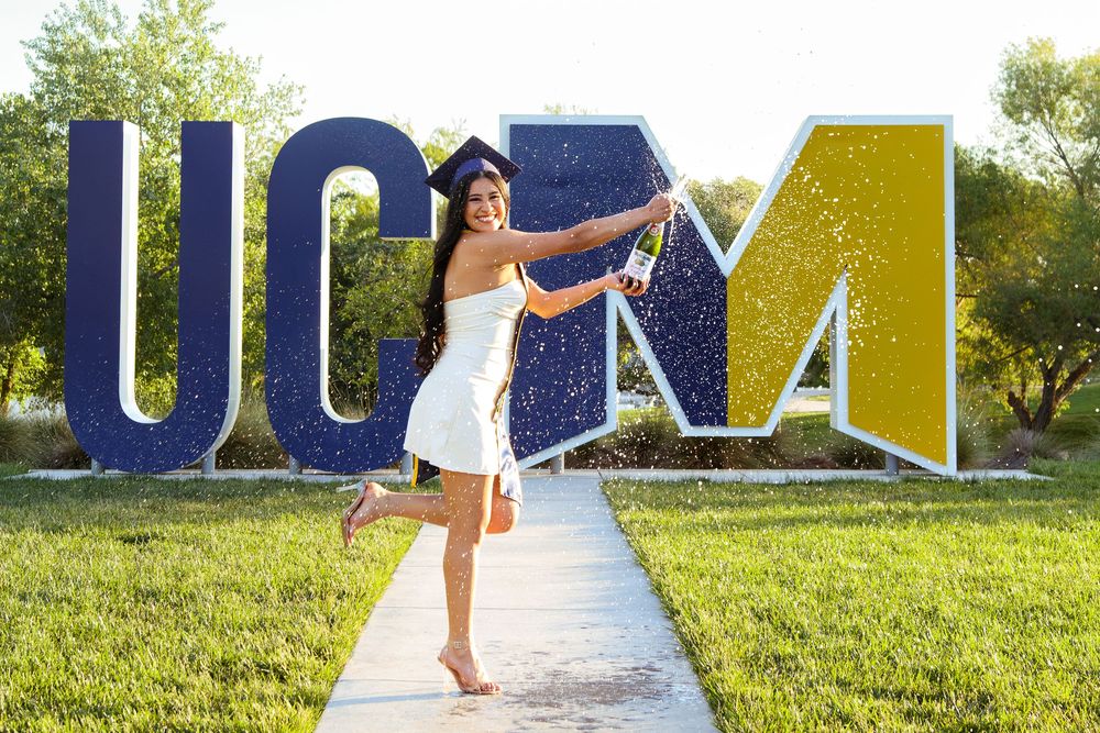 Graduate celebrating in front of large UCM letter sign outdoors.