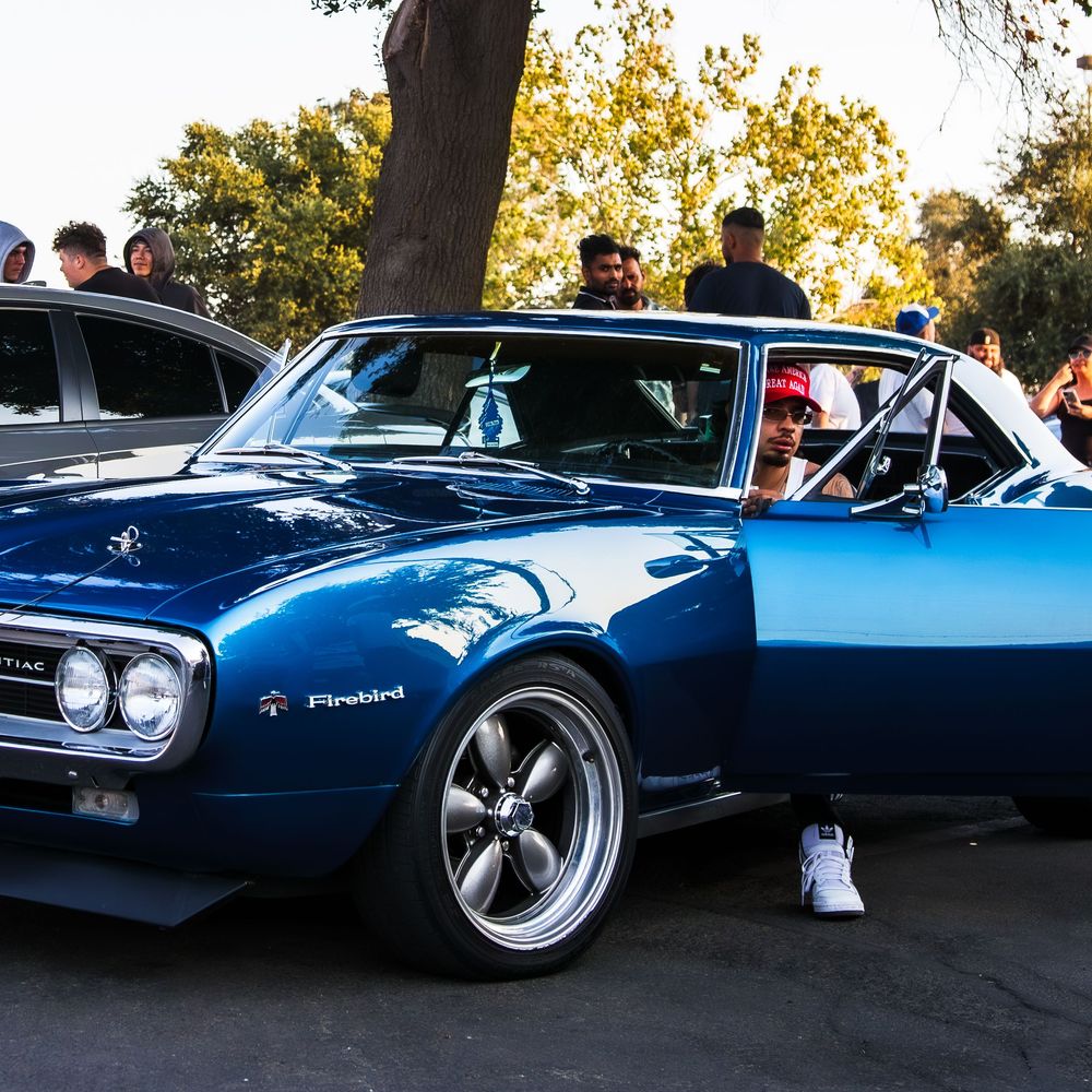 Classic blue Pontiac Firebird muscle car on display at an outdoor car show.