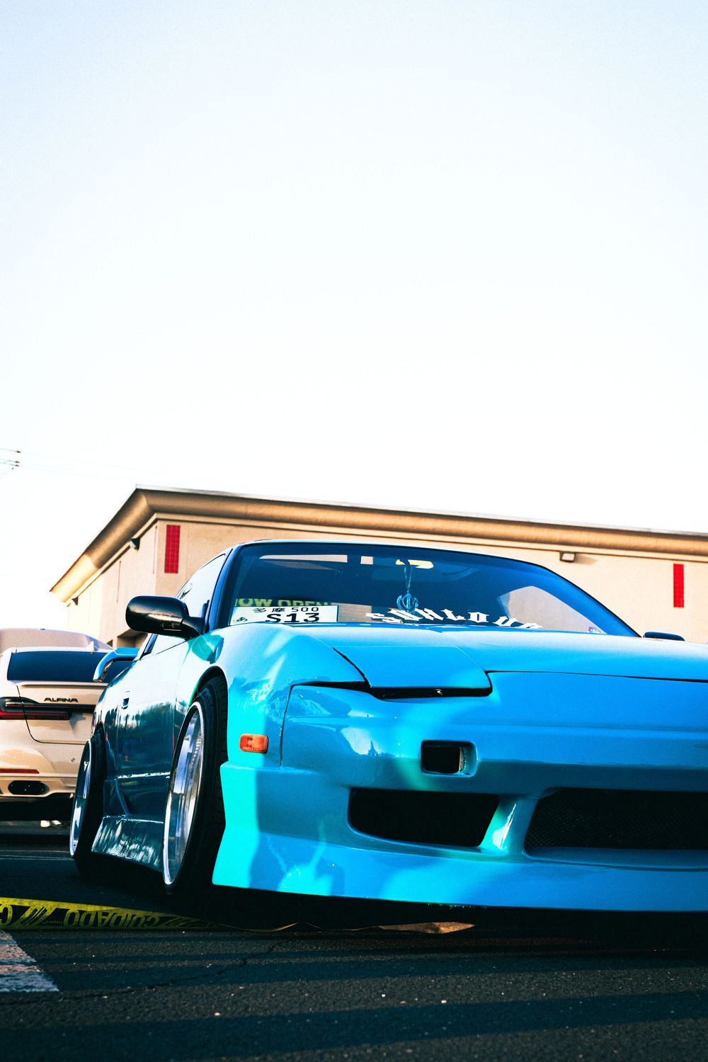 Bright cyan modified sports car with custom body kit parked in a lot.
