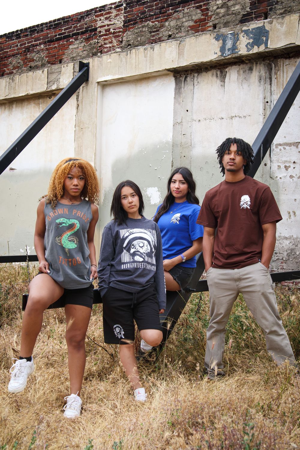 Four young adults in streetwear posing together outdoors near an old building.