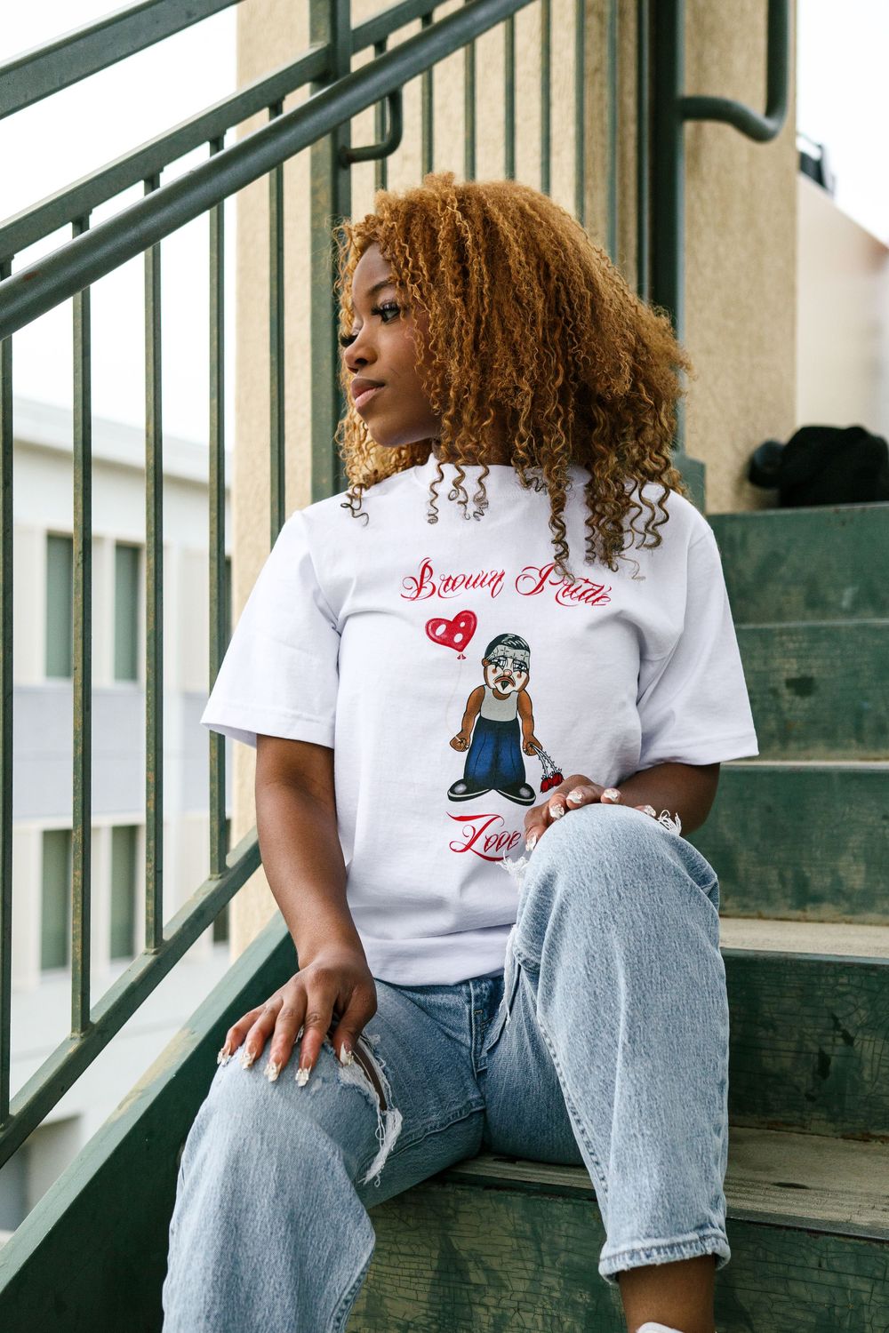 Young woman in white graphic tee and jeans sitting on outdoor stairs.