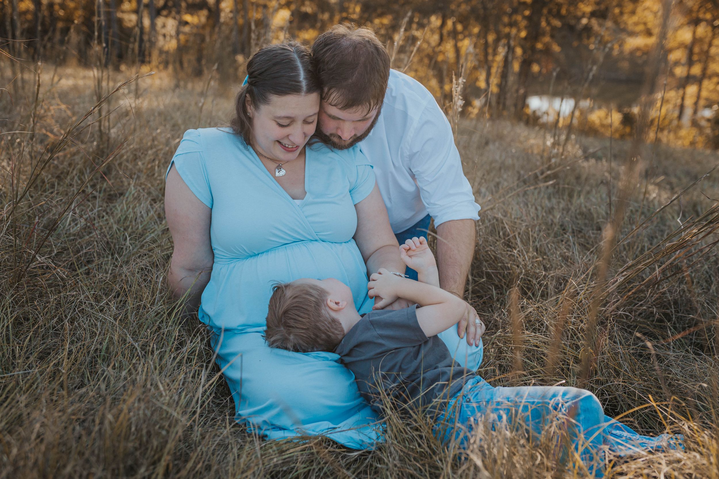 A couple in blue and white sits together in a golden field during sunset while sharing an intimate moment.