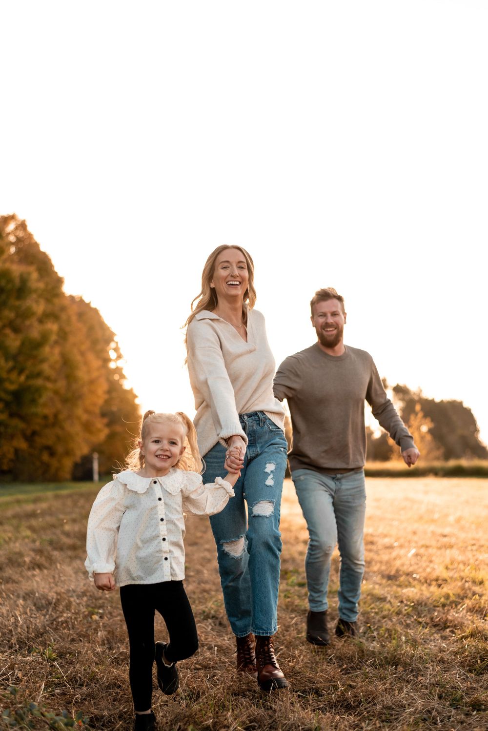 Family walks together through golden autumn field at sunset in casual attire enjoying outdoor time together.