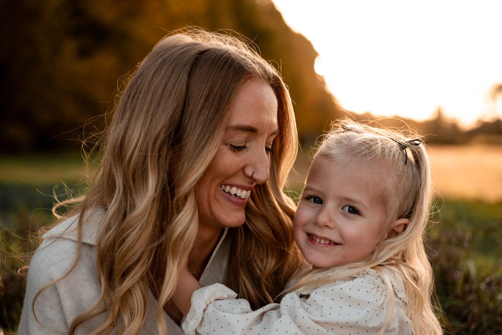 A mother and daughter share a joyful moment together outdoors during golden hour sunset.