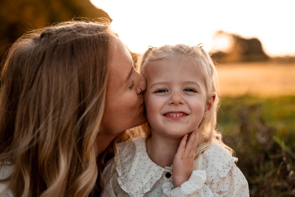 A tender moment between parent and child sharing a kiss outdoors during golden hour.