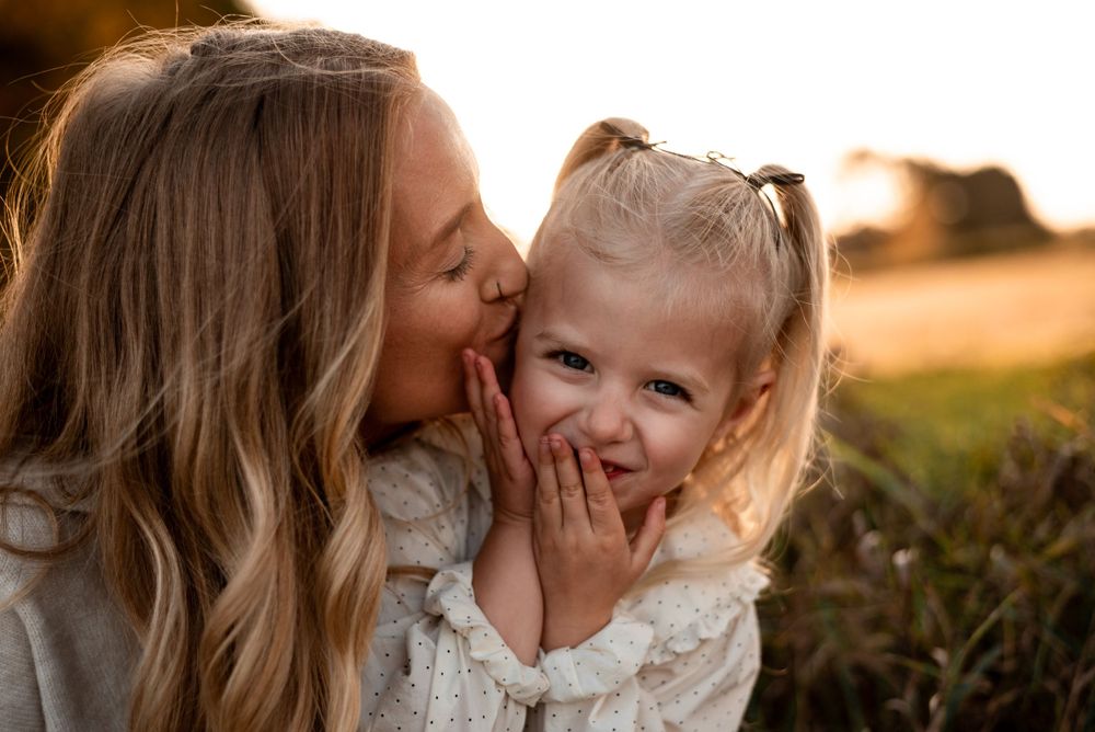 A joyful moment between parent and child sharing laughter in a golden sunlit field at sunset.