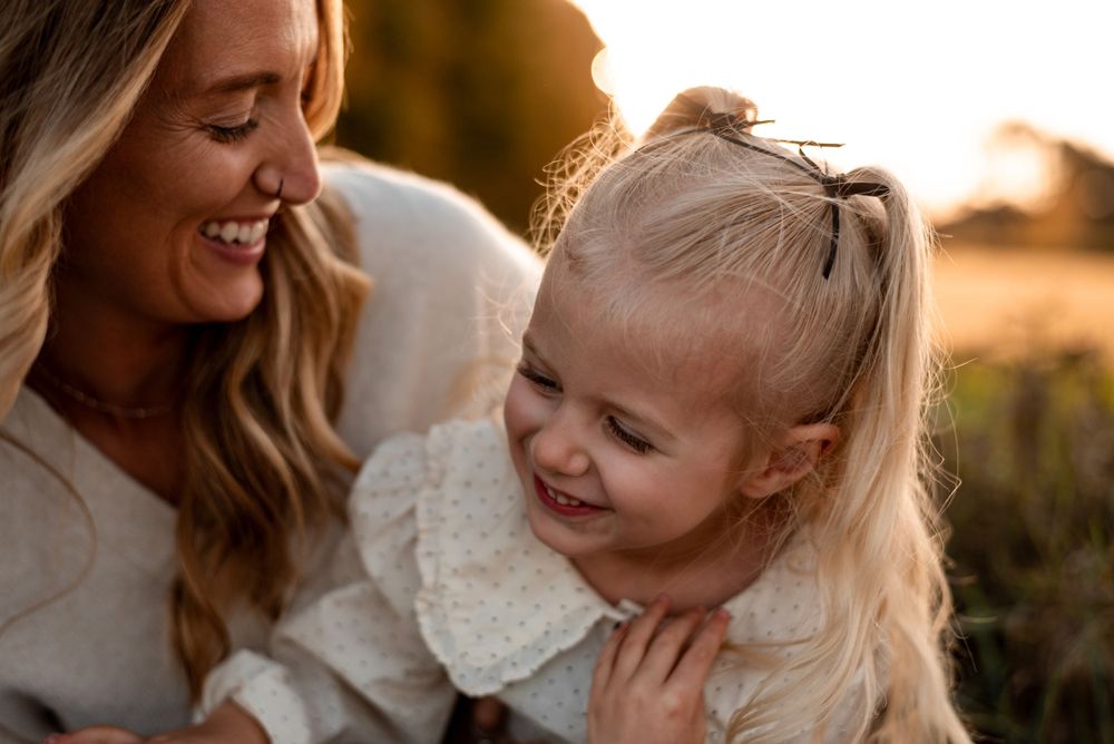A heartwarming moment of joy between parent and child laughing together at sunset in a field.