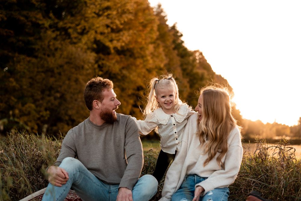 A family sits together in a sunlit field surrounded by autumn trees during golden hour at sunset.