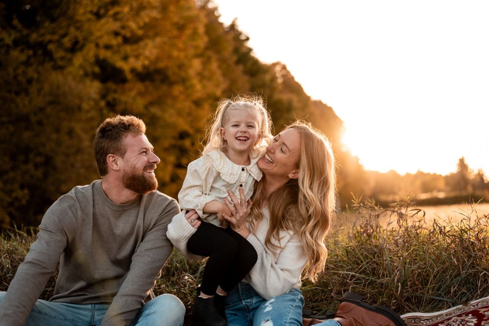 A family shares joyful laughter together during golden hour in a sunlit meadow field.