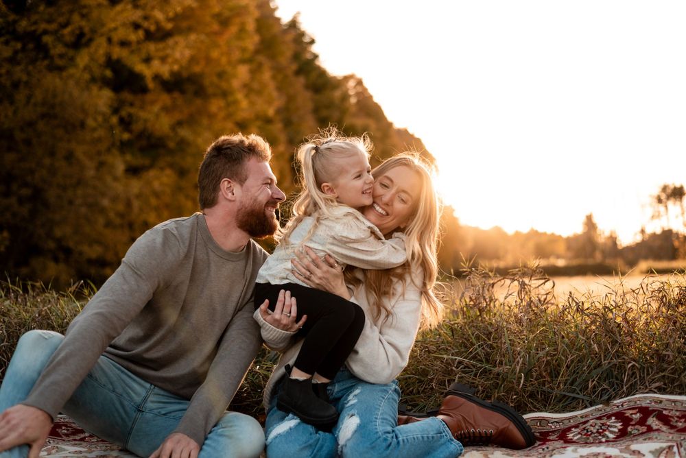 A family enjoys a playful moment together on a blanket during golden hour in a field at sunset.