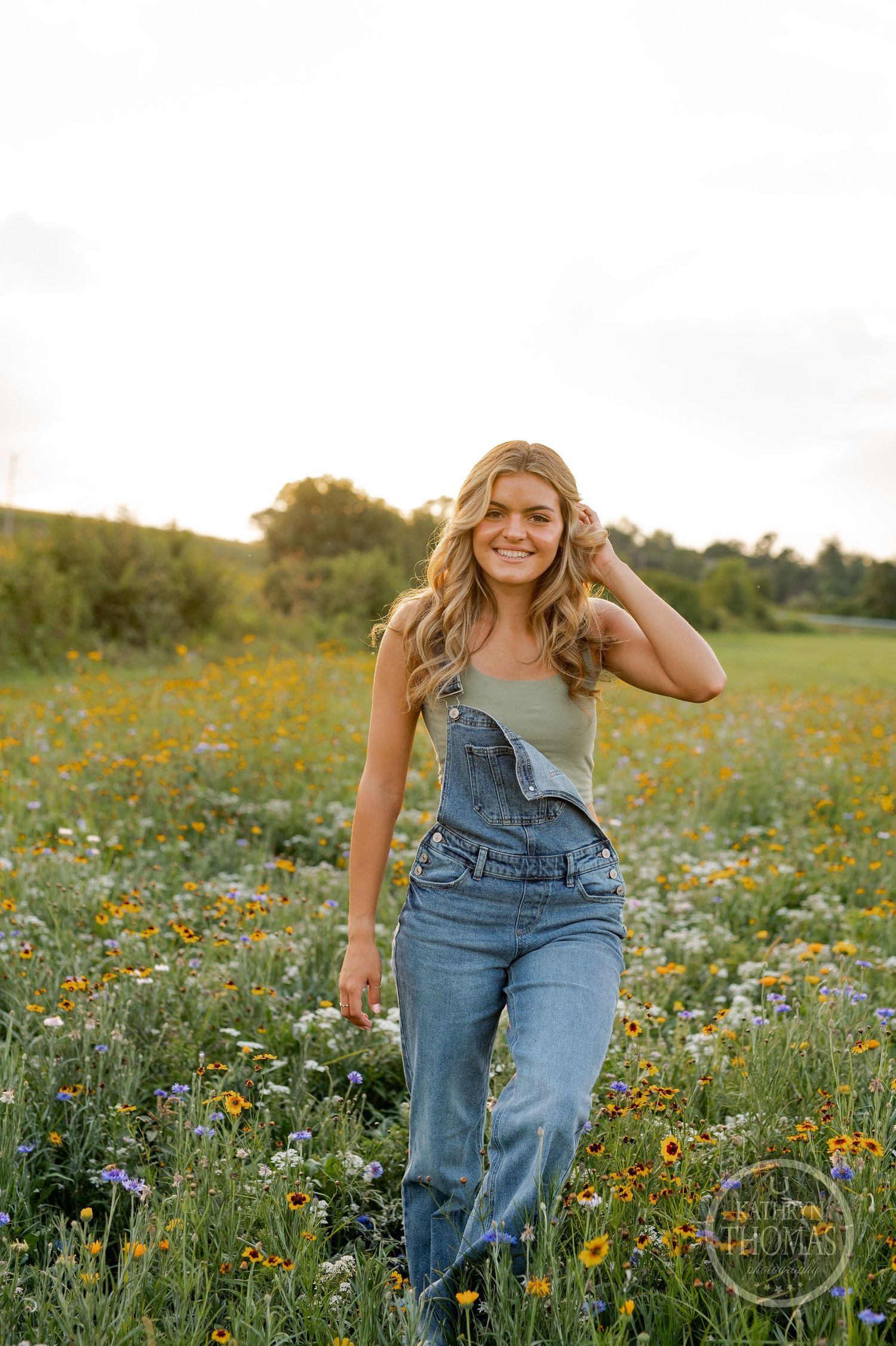 Someone walking through a wildflower meadow wearing overalls and a sage green tank top.