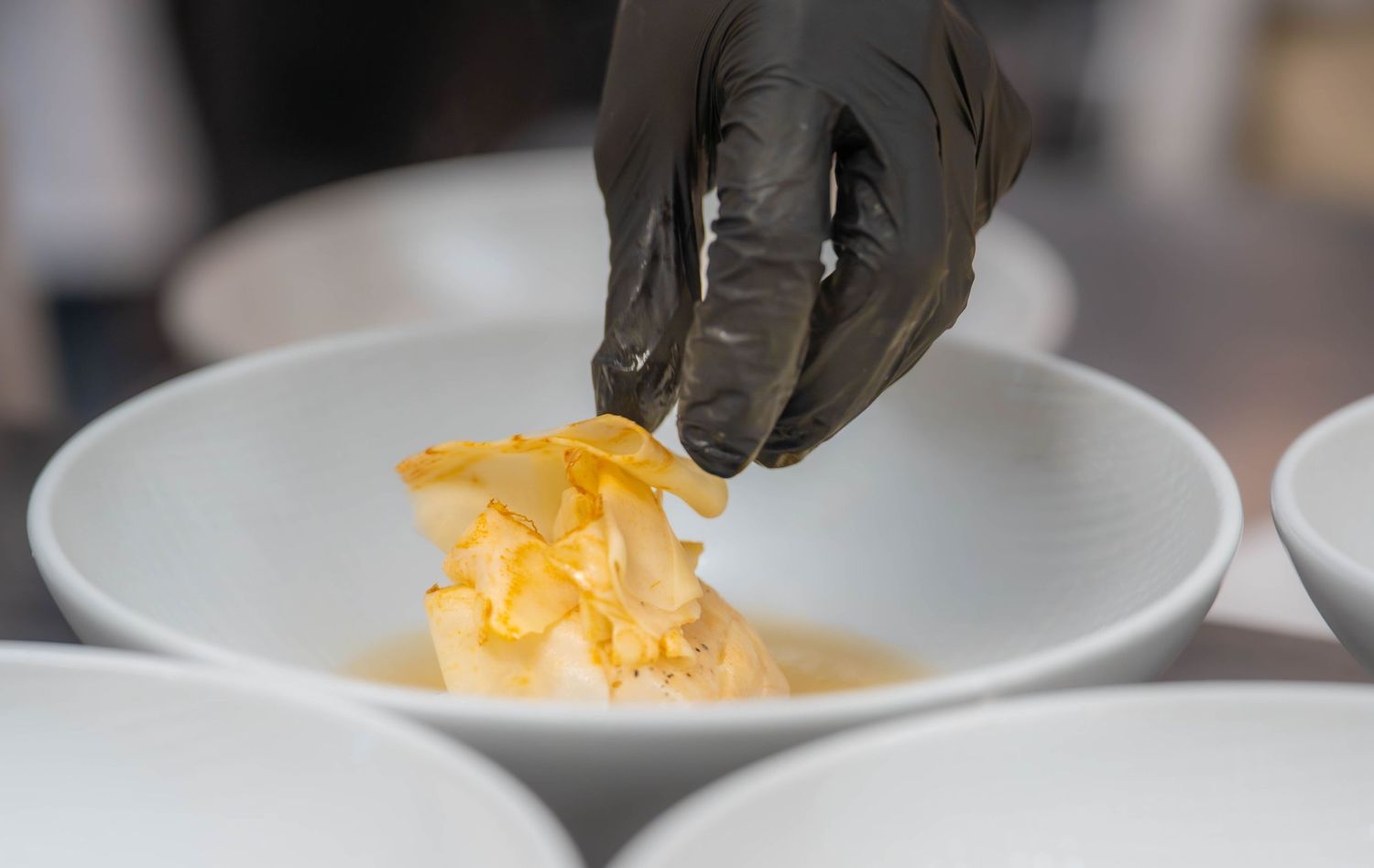 Grated orange cheddar cheese being sprinkled onto a white plate in a restaurant kitchen setting.  Food product photography Quad Cities.