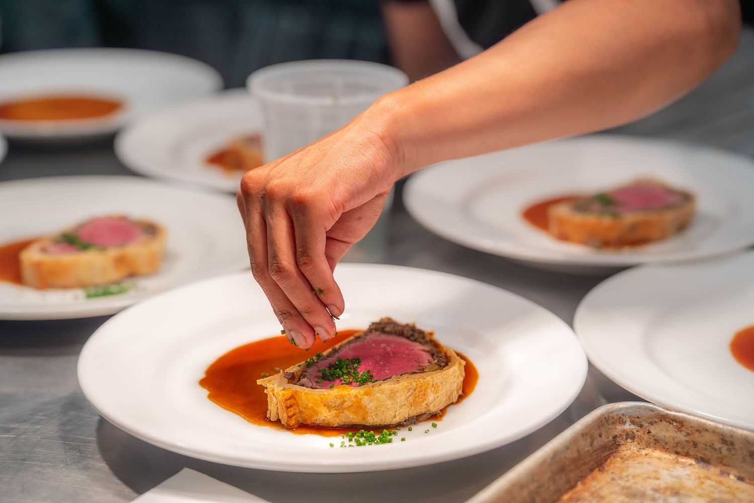 Chef plating multiple dishes with red sauce and garnishes on white plates in a professional kitchen.  Food product photography Quad Cities.