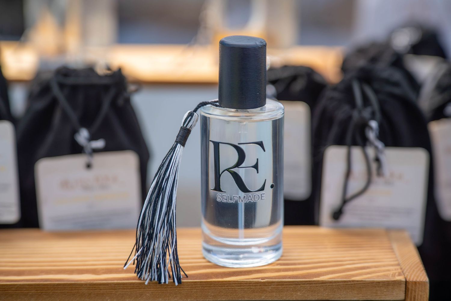 Elegant RE perfume bottle with tassel on wooden shelf, surrounded by black gift bags in a luxury store. Quad Cities Product Photography