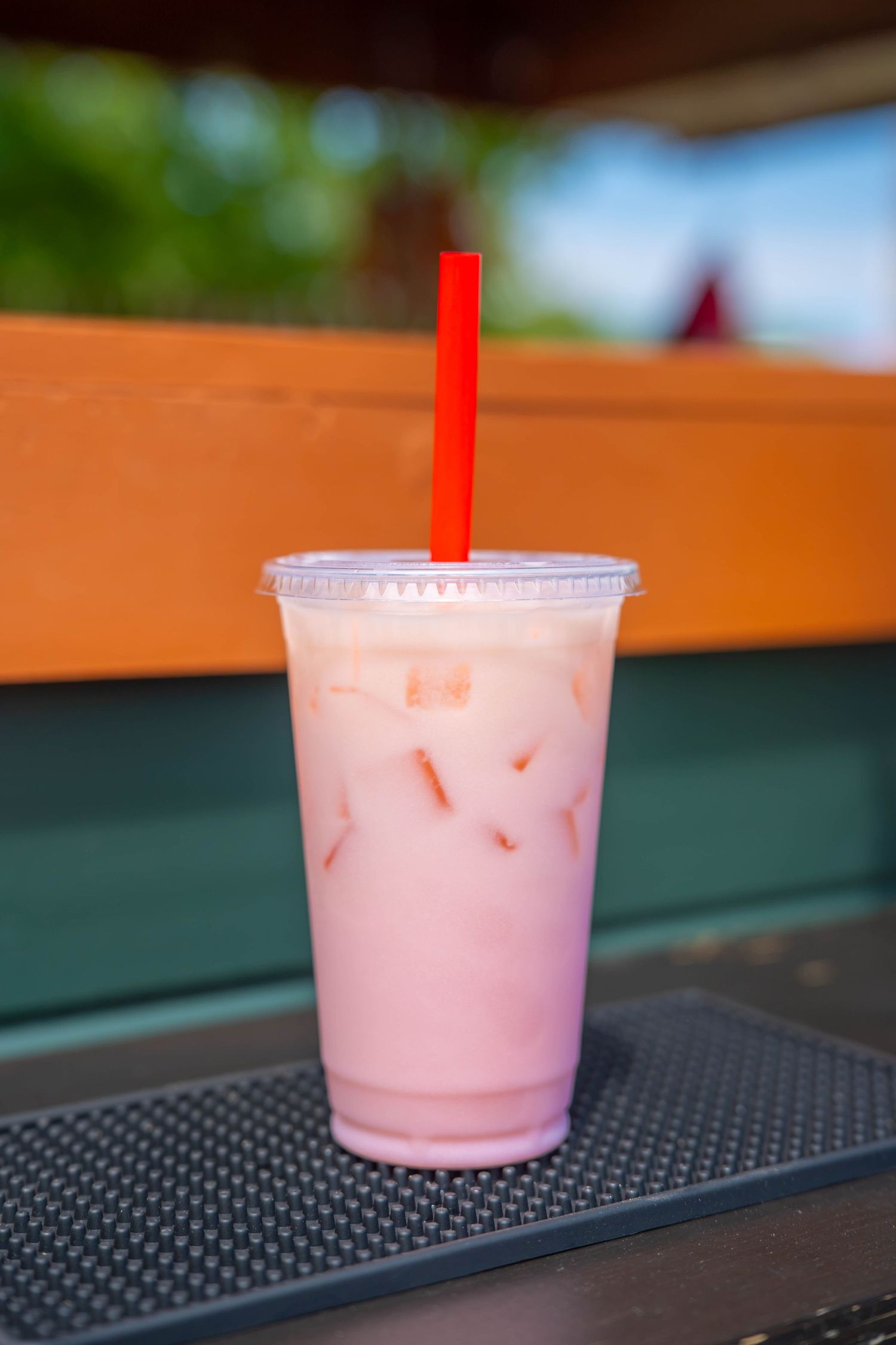 A refreshing iced pink strawberry milk drink in a plastic cup with a red straw on a black tray outdoors. Quad Cities Product Photography