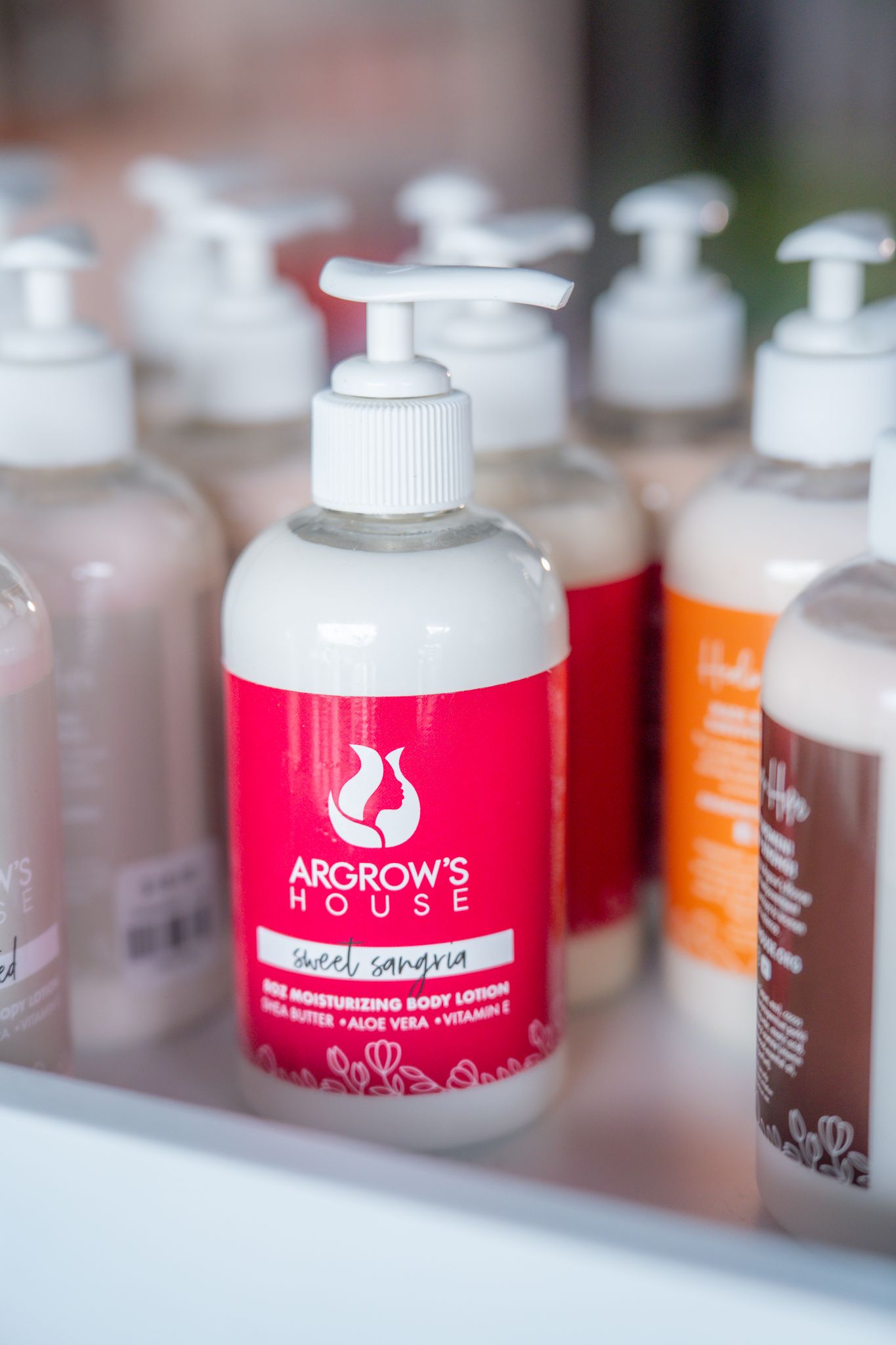 Argrow's House body lotion pump bottle with white logo amongst other beauty products on shelf. Quad Cities Product Photography