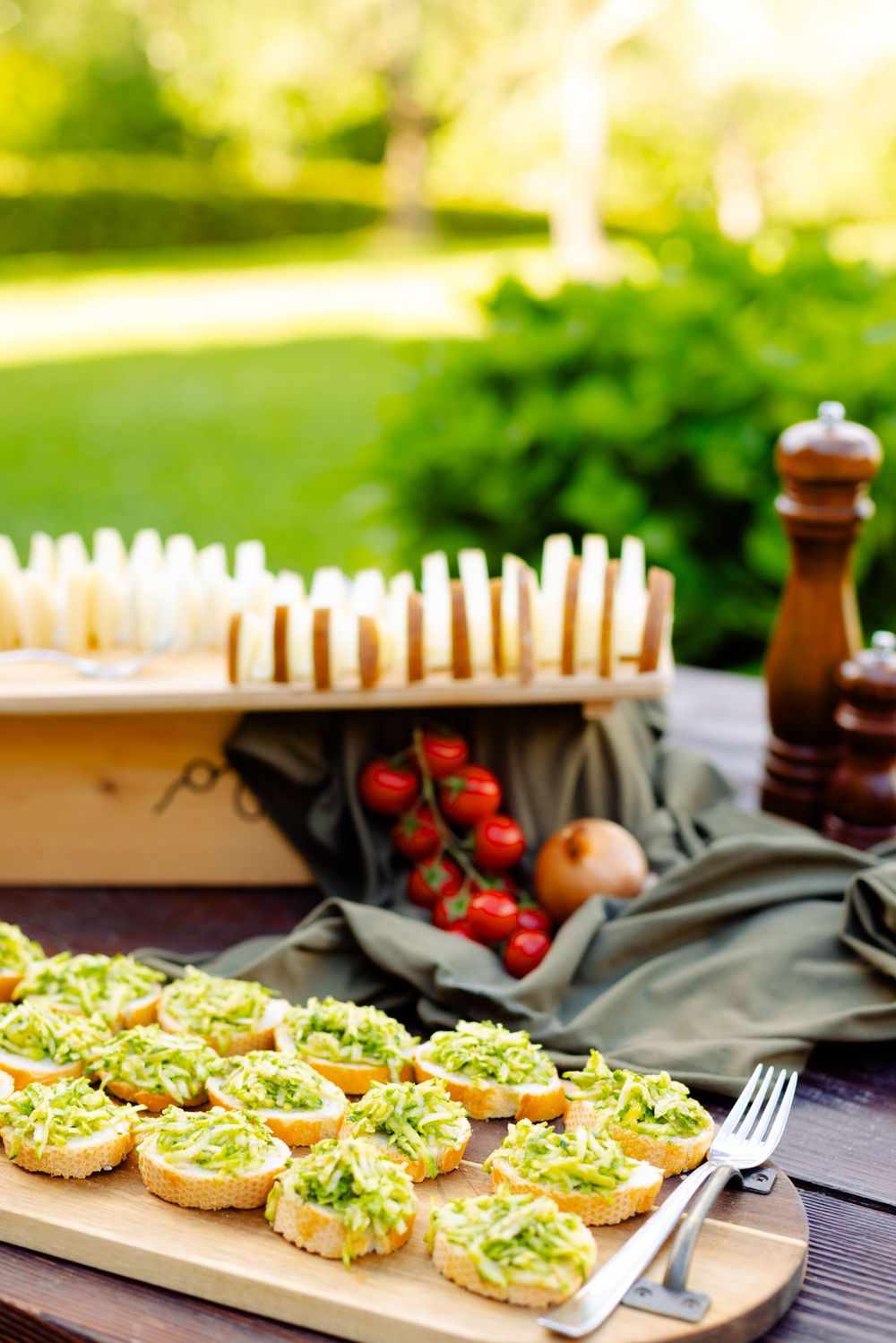 Appetizer platter with avocado toast bites and fresh tomatoes on outdoor wooden table.