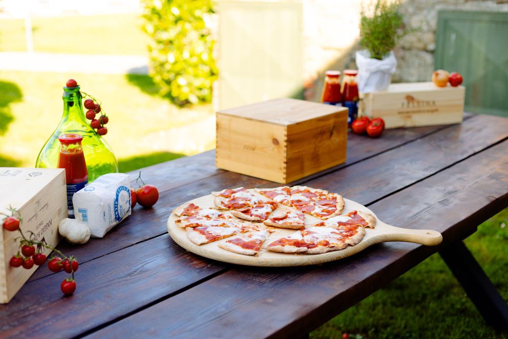 Pizza and wooden boxes arranged on rustic outdoor picnic table with string lights.