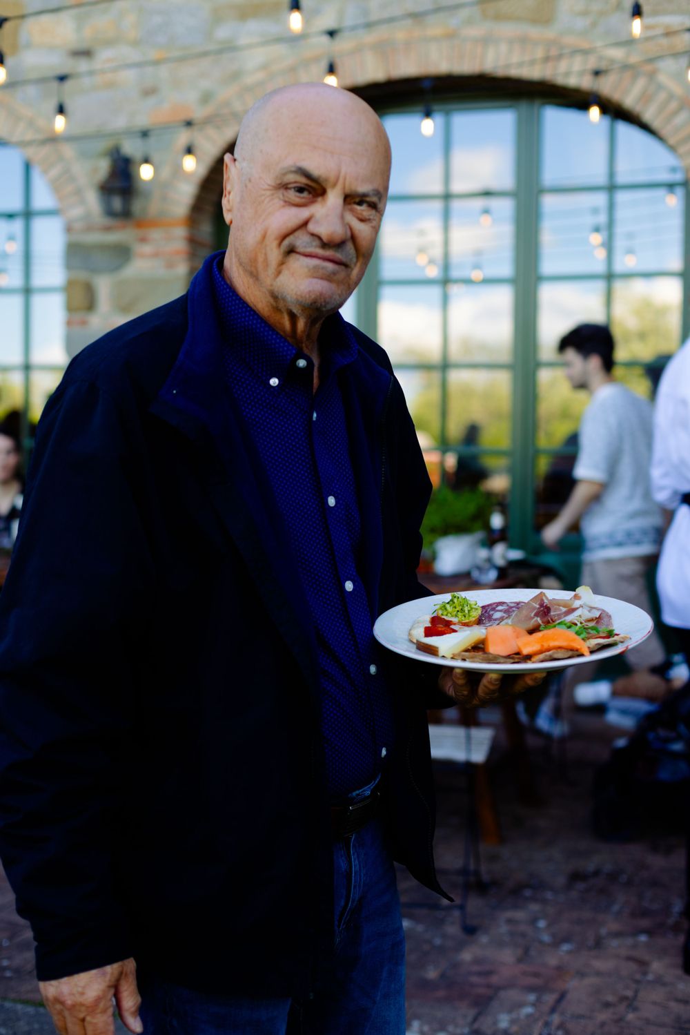 Person holding plate of food at stone-arched restaurant patio.