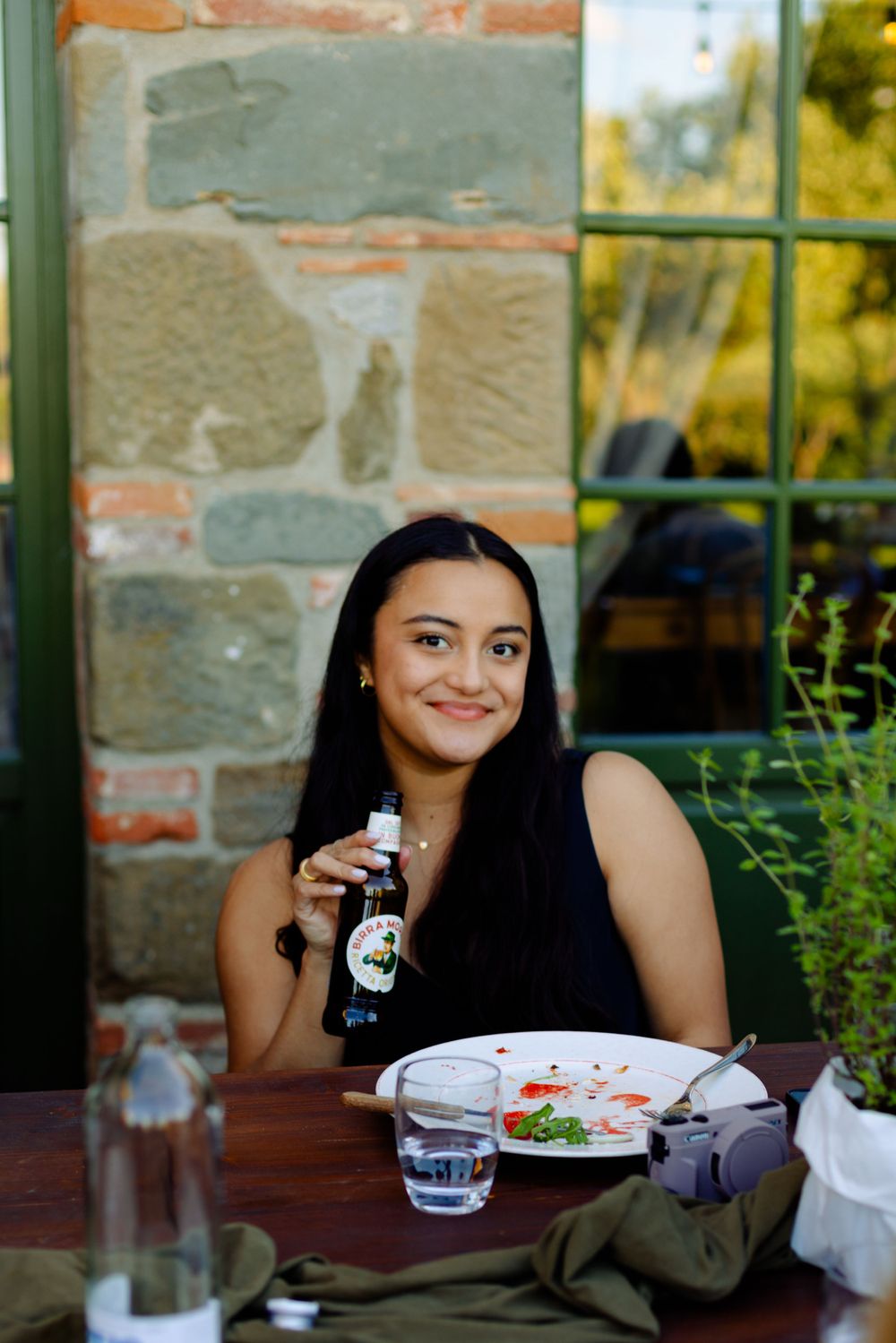 A diner enjoys a meal and beverage on a stone patio with greenery in the background.
