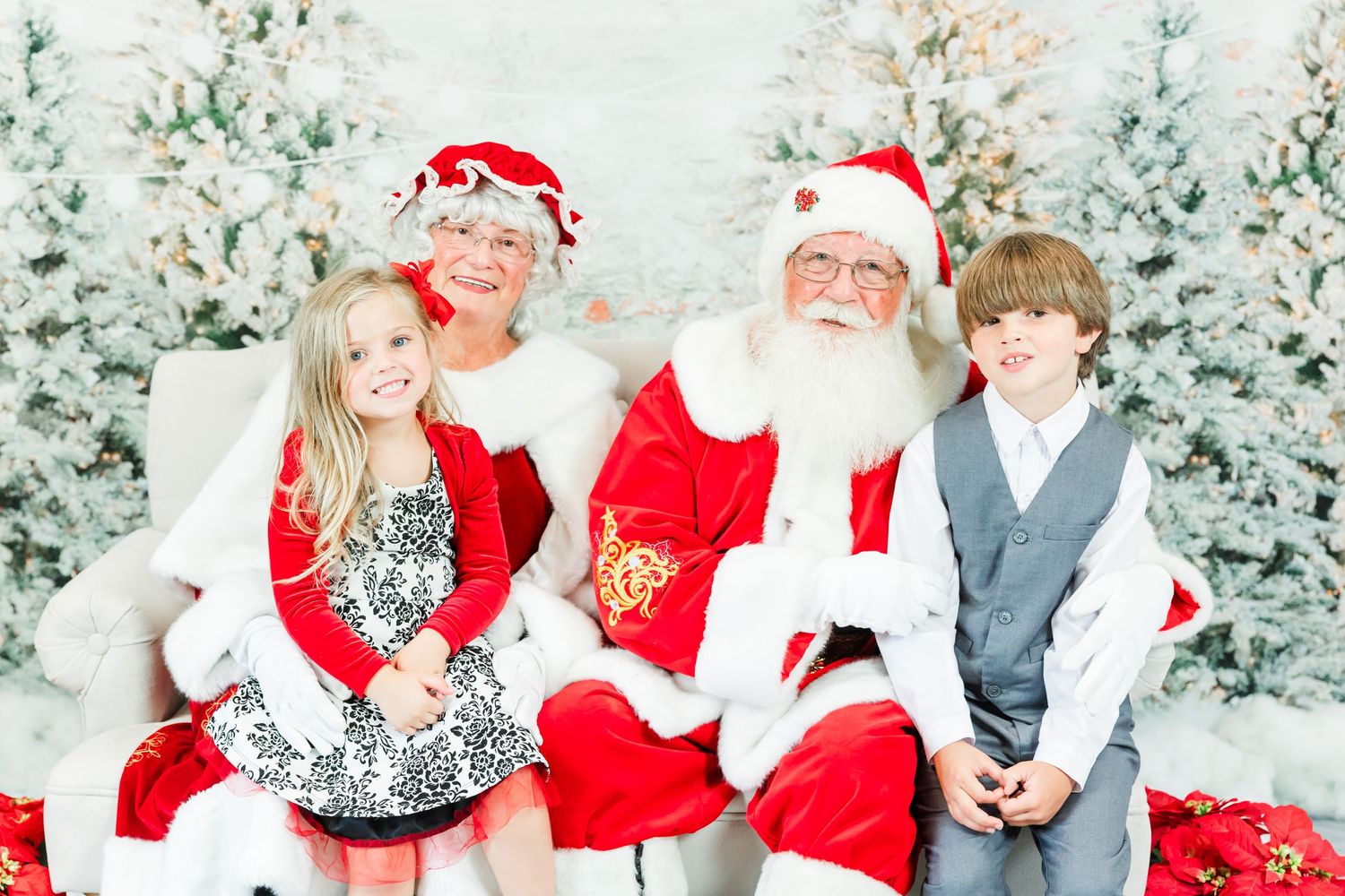 Children visiting Santa Claus in a festive winter wonderland setting with snow-covered trees in the background.