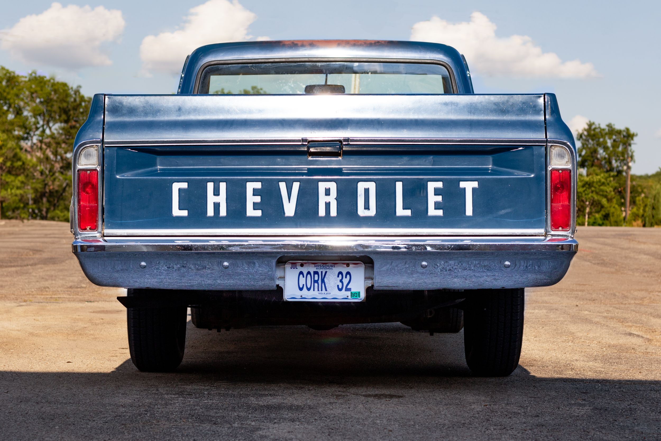 Close-up view of a vintage blue Chevrolet pickup truck tailgate against a sunny outdoor background.