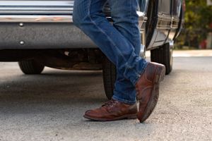 Close-up of feet and legs near classic cars showing brown boots and sandals.