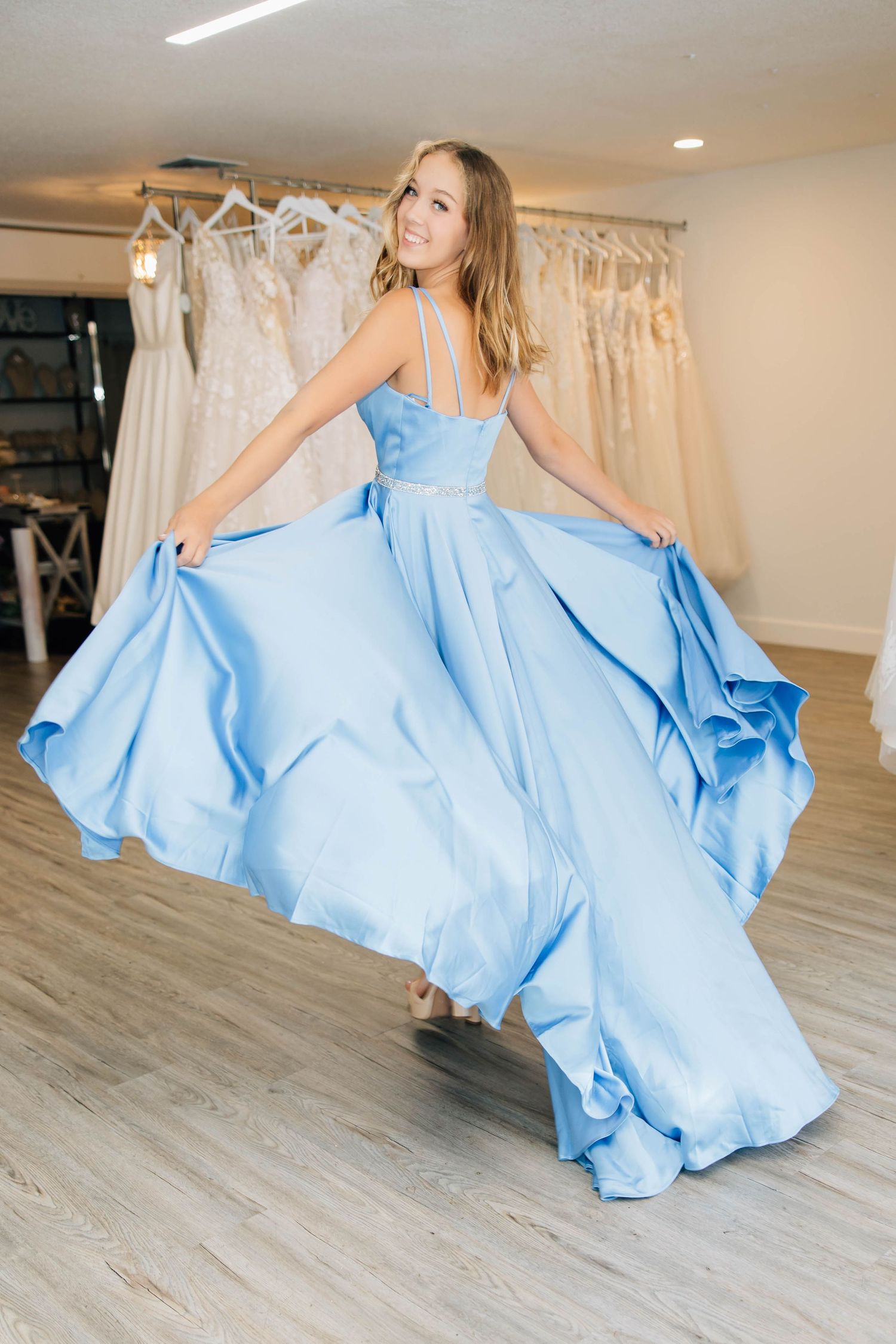 Woman twirling in voluminous light blue ballgown with spaghetti straps in bridal boutique.