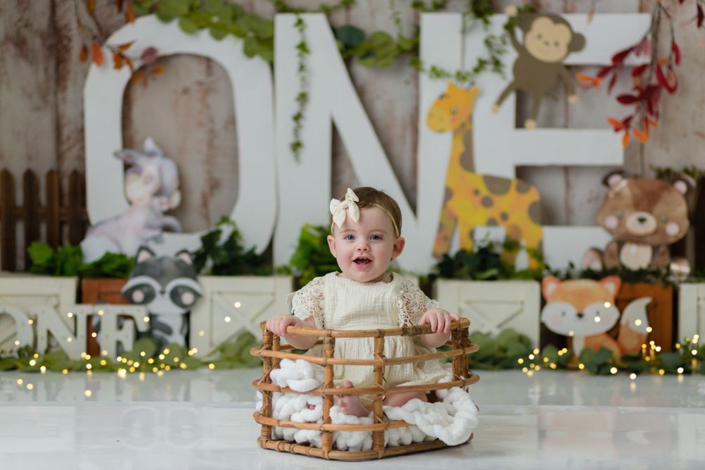 A happy toddler sits in a wooden basket prop with large decorative letters and giraffe in background.
