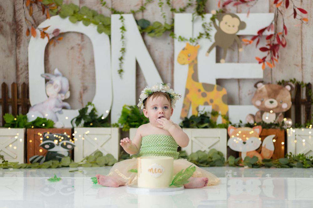 First birthday cake smash session with woodland theme backdrop and green accents.