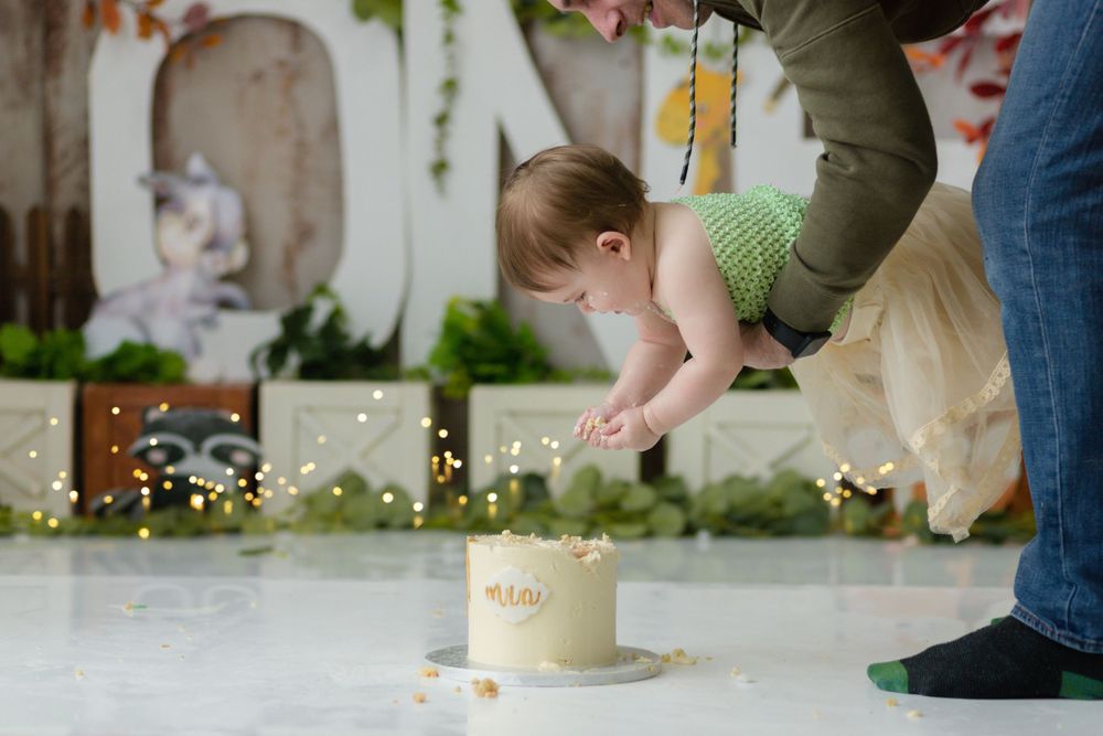 Small cake on floor with woodland themed backdrop and decorative elements.