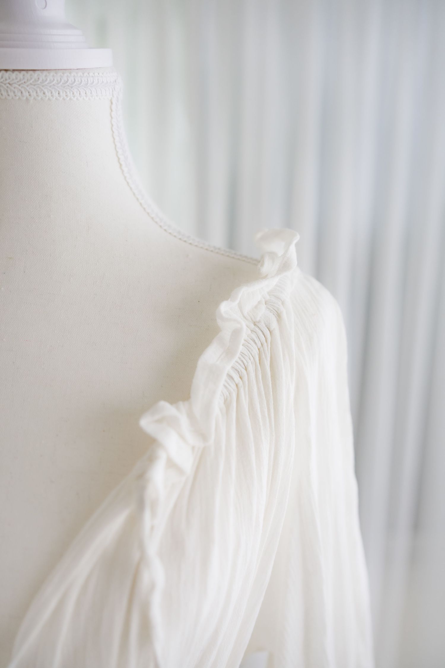 Detailed view of white dress fabric showing intricate pleating and ruffle details.