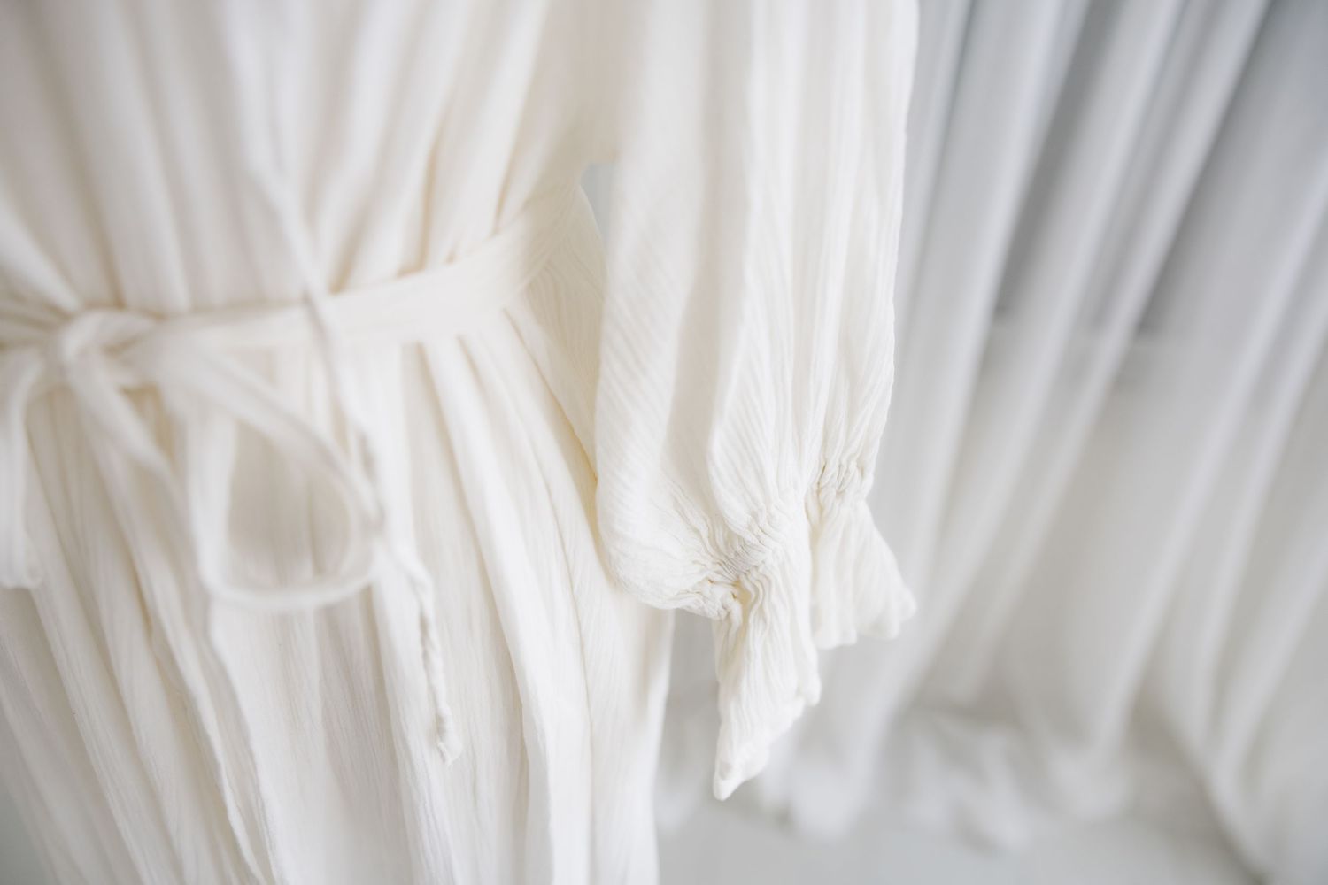 Close-up detail of delicate white fabric pleats and tie belt on a dress.