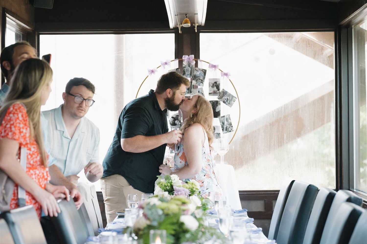 A couple shares a tender moment at an elegantly decorated engagement reception table with floral centerpieces.