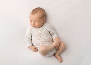 Sleeping newborn in light gray knit outfit lying on white background.
