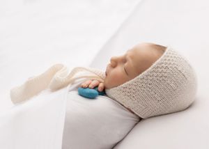 Sleeping newborn in knit wrap with blue accent on white background.
